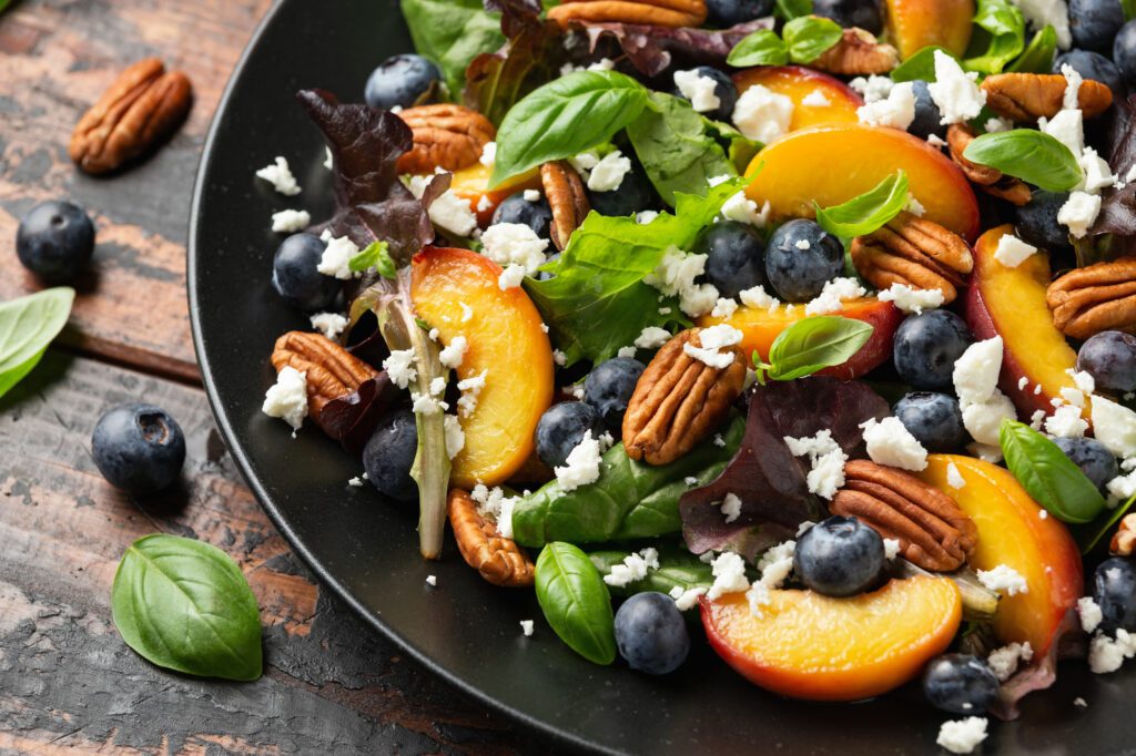 Healthy peach and blueberry salad with leafy greens and pecan nuts. 